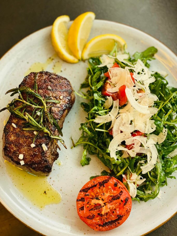 Gegrilltes Steak mit Rosmarin, frischem Salat, Tomate und Zitronenscheiben.