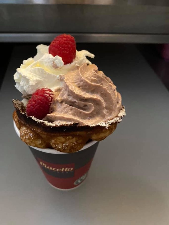 Eisbecher mit Schokoladeneis, Sahne und Himbeeren in einer Waffel.